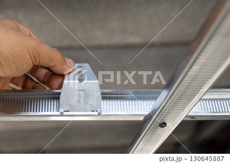 Worker is using locking keys to lock top cross rails to furring channels in concealed ceiling Worker is using locking keys to lock top cross rails to furring channels in concealed ceiling 130645887