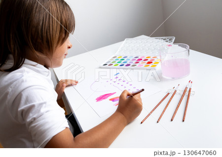 Young caucasian child painting with watercolors at a white table Young caucasian child painting with watercolors at a white table 130647060