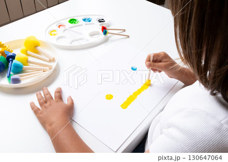Young child painting with bright colors using sponges and sticks on white paper at home Young child painting with bright colors using sponges and sticks on white paper at home 130647064