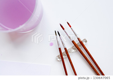 Assorted artist brushes with glass of purple water on white canvas 130647065