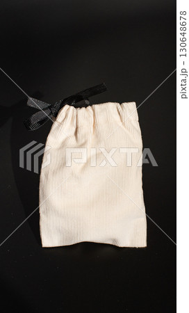 Small white fabric pouch with black bow on black background 130648678