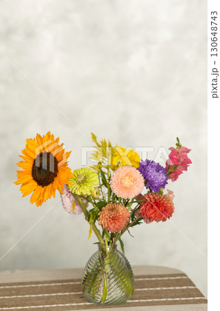 Vibrant bouquet of mixed flowers in glass vase on striped tablecloth Vibrant bouquet of mixed flowers in glass vase on striped tablecloth 130648743