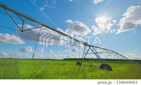 The irrigation system is operating in a lush green field that is situated beneath a bright sky 130649003