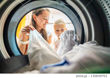 Mother and daughter doing laundry together in a self-service public laundromat, sharing household chores, building responsibility and cooperation in everyday family routine Mother and daughter doing laundry together in a self-service public laundromat, sharing household chores, building responsibility and cooperation in everyday family routine 130649701