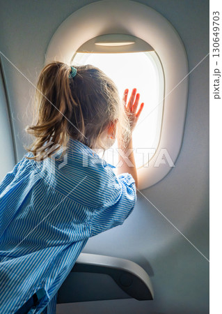 Little girl looking out the airplane window during a flight. Wonder, travel experience, and childhood curiosity in the air. Little girl looking out the airplane window during a flight. Wonder, travel experience, and childhood curiosity in the air. 130649703