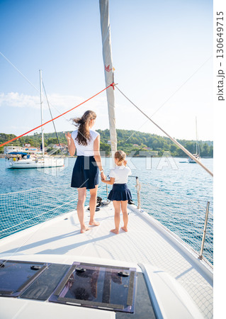 Mother and daughter spending time together on the bow of a sailing yacht. Family bonding, sea adventure, and peaceful travel lifestyle 130649715