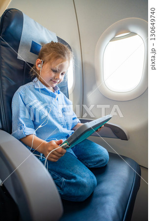 Little girl watching a cartoon on a tablet with headphones during an airplane flight. Digital entertainment, child focus, and quiet family travel experience. Little girl watching a cartoon on a tablet with headphones during an airplane flight. Digital entertainment, child focus, and quiet family travel experience. 130649740