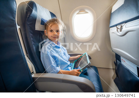 Little girl watching a cartoon on a tablet with headphones during an airplane flight. Digital entertainment, child focus, and quiet family travel experience. Little girl watching a cartoon on a tablet with headphones during an airplane flight. Digital entertainment, child focus, and quiet family travel experience. 130649741