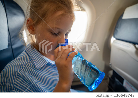 Little girl drinking water from a plastic bottle during a flight. In-flight hydration, travel routine, and caring for body needs while flying Little girl drinking water from a plastic bottle during a flight. In-flight hydration, travel routine, and caring for body needs while flying 130649748