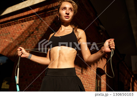 Young athletic woman jumps rope outdoors against a brick building background 130650103