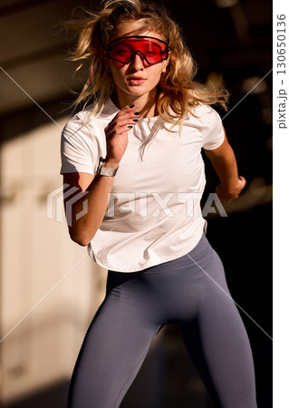Athletic woman running outdoors in the sunlight wearing red sport sunglasses 130650136