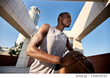 Athletic man stretching outdoors with modern architecture and clear sky backdrop 130650182