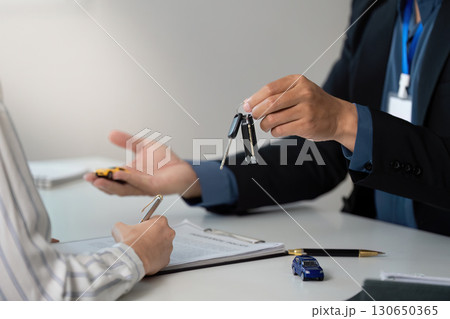 Key Handover. Professional presenting car keys to client during insurance consultation. 130650365