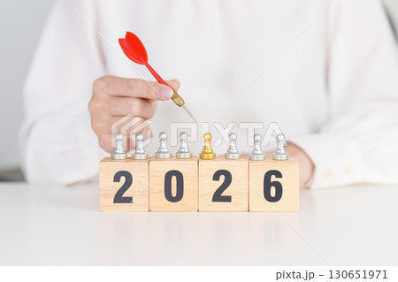 Hand holding red dart over people chess and 2026 year blocks. Goal, plan, action, target, strategy, leadership, New Year and marketing concept 130651971