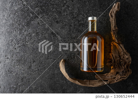 Bottle of whiskey and old snags on a black stone background. 130652444