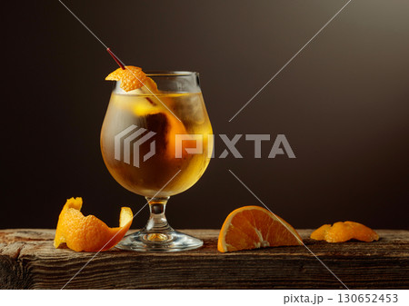 Old Fashioned cocktail with a ice, garnished with an orange peel on a old wooden board. Old Fashioned cocktail with a ice, garnished with an orange peel on a old wooden board. 130652453