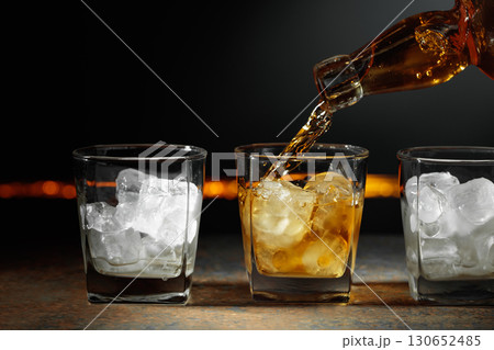 Whiskey is poured into a glass with ice. Whiskey is poured into a glass with ice. 130652485