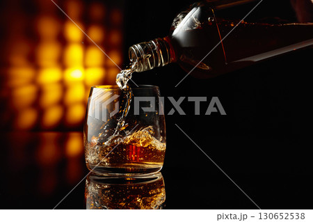 Pouring whiskey from a bottle into a glass. Pouring whiskey from a bottle into a glass. 130652538