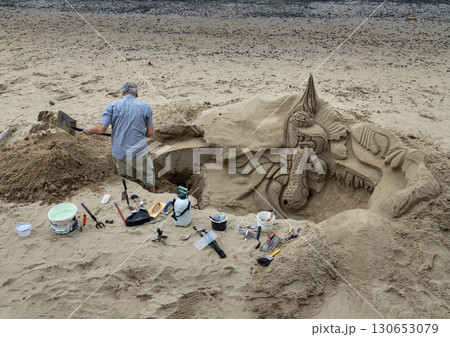 a sand artist at working on a detailed sand sculpture on a small beach. a sand artist at working on a detailed sand sculpture on a small beach. 130653079