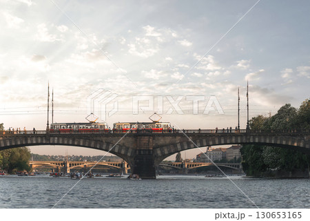 Trams crossing a bridge over the Vltava river in Prague while rowers enjoy the water. Czech Republic 130653165