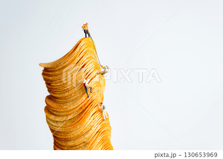Miniature people climbing a huge stack of potato chips representing hard work and success Miniature people climbing a huge stack of potato chips representing hard work and success 130653969