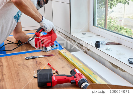 repairman using electric jigsaw and cutting hole for the sink in the kitchen countertops 130654071