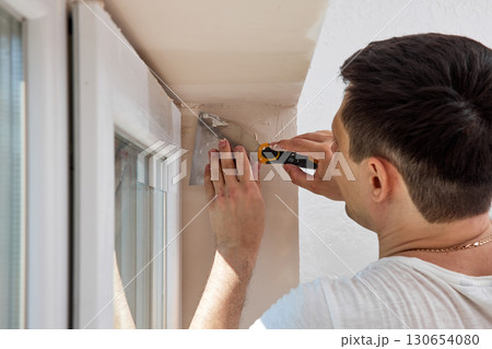Caucasian plasterer man with a spatula applying finishing putty on a window opening 130654080