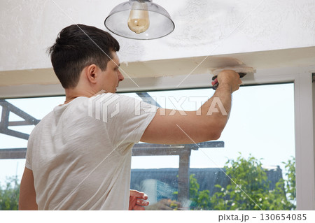 Caucasian plasterer man with a spatula applying finishing putty on a window opening 130654085