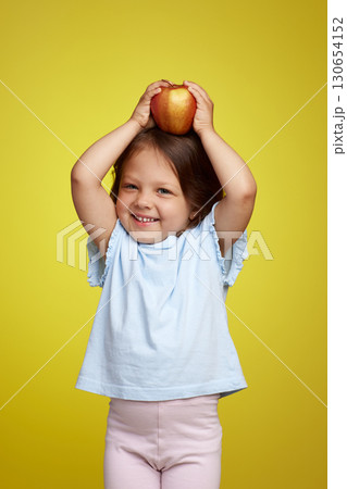 cute Caucasian little child girl holding apple on yellow background 130654152