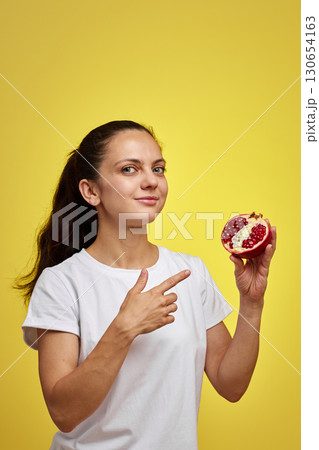 Beautiful happy woman holding pomegranate on yellow background Beautiful happy woman holding pomegranate on yellow background 130654163