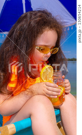 Close up of girl sipping orange juice with lemon slice in summer beach setting 130654214