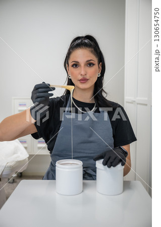 Beautician woman in black gloves holding jar of sugaring paste for hair removal procedure 130654750