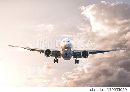 Modern passenger airplane flying in cloudy sky at sunset 130655029