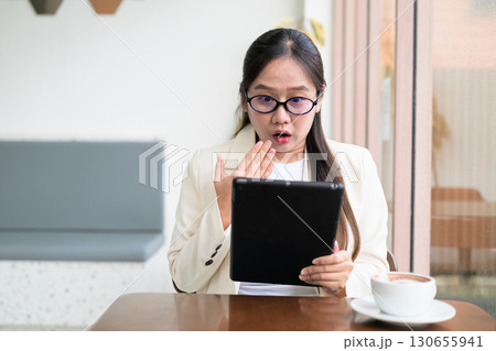 Asian businesswoman sitting in cafe using digital tablet computer looking shocked and surprised 130655941