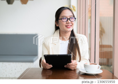 Asian cute woman sitting in coffee shop using tablet computer looking through window and thinking Asian cute woman sitting in coffee shop using tablet computer looking through window and thinking 130655950