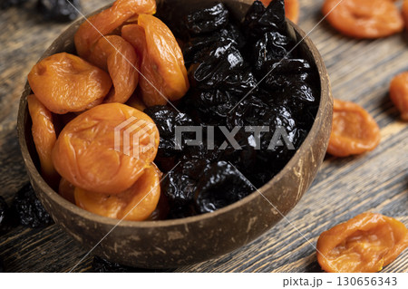 dried apricots and prunes made from ripe blue plums mixed together in a plate , dried plums and apricots in a bowl made from natural materials 130656343