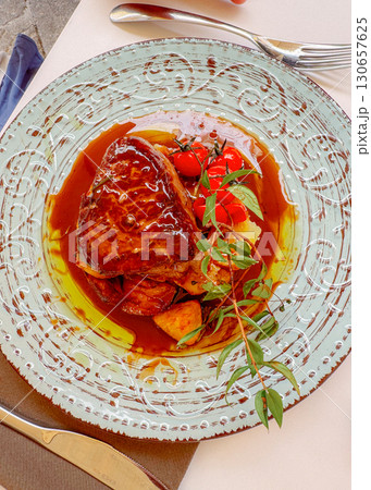 Gourmet steak dish served with roasted potatoes and cherry tomatoes garnished with fresh herbs. A rich sauce enhances the exquisite presentation on a decorative plate. 130657625