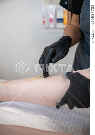Beautician applying sugaring paste on female leg during professional hair removal procedure Beautician applying sugaring paste on female leg during professional hair removal procedure 130657782