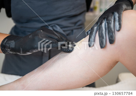 Beautician applying sugaring paste on female leg during professional hair removal procedure 130657784
