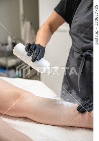 Beautician applying talcum powder on female leg before professional hair removal procedure 130657785