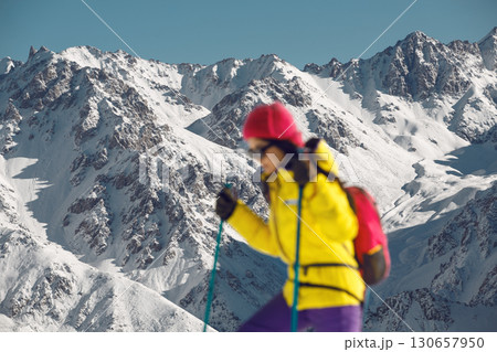 Blurred Woman Ascends Snow-Covered Slope Under Bright Winter Sunlight in Mountainous Terrain Blurred Woman Ascends Snow-Covered Slope Under Bright Winter Sunlight in Mountainous Terrain 130657950