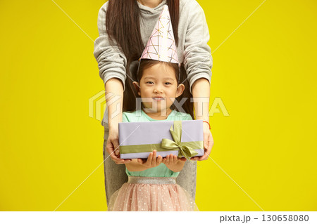 Gift Time: Joyful Birthday Girl Holding a Present from loving mother, close up photo against yellow isolated. Gift Time: Joyful Birthday Girl Holding a Present from loving mother, close up photo against yellow isolated. 130658080