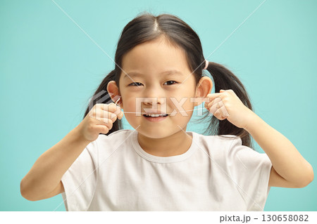Lovely five years old chinese girl cleans herself teeth by means dental floss, headshot portrait on blue isolated.  130658082