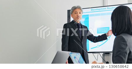大画面モニターの前で説明するミドルエイジ男性ビジネスパーソン 130658642