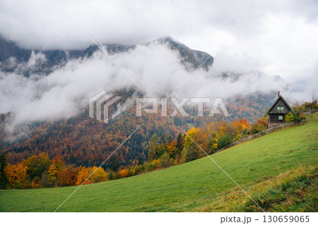 Autumn colors surround a cabin in Slovenia, with mountains shrouded in mist Autumn colors surround a cabin in Slovenia, with mountains shrouded in mist 130659065