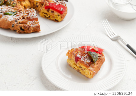 A slice of holiday cake with candied fruit on a white plate, with the rest of the cake in the background A slice of holiday cake with candied fruit on a white plate, with the rest of the cake in the background 130659124