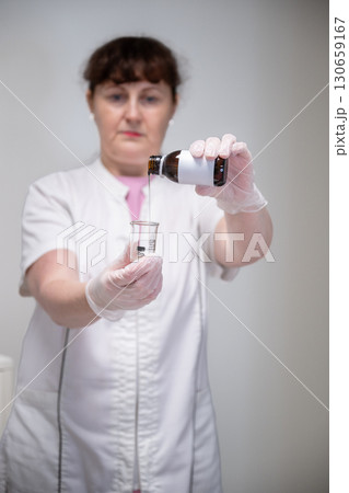 Beautician pouring cosmetic liquid from brown glass bottle into measuring beaker in salon Beautician pouring cosmetic liquid from brown glass bottle into measuring beaker in salon 130659167