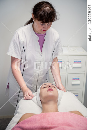 Beautician preparing female client for cosmetic facial treatment in professional beauty salon 130659168