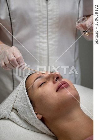 Beautician applying cosmetic treatment on female face with cotton swab in beauty salon 130659172
