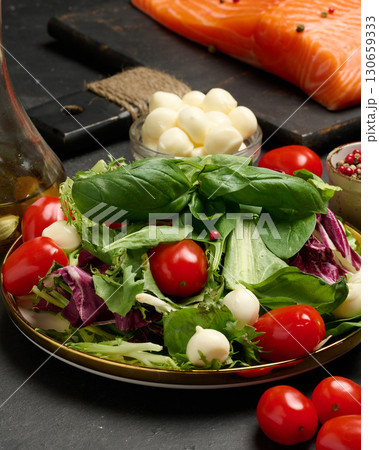 Close-up of a plate with fresh lettuce, cherry tomatoes, mozzarella balls and basil leaves. 130659333